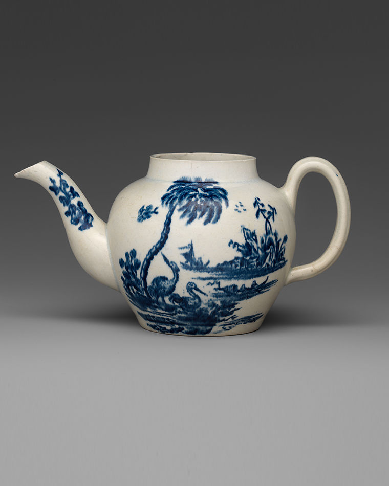 A white teacup with dark blue paintings of palm trees and an island in the background.